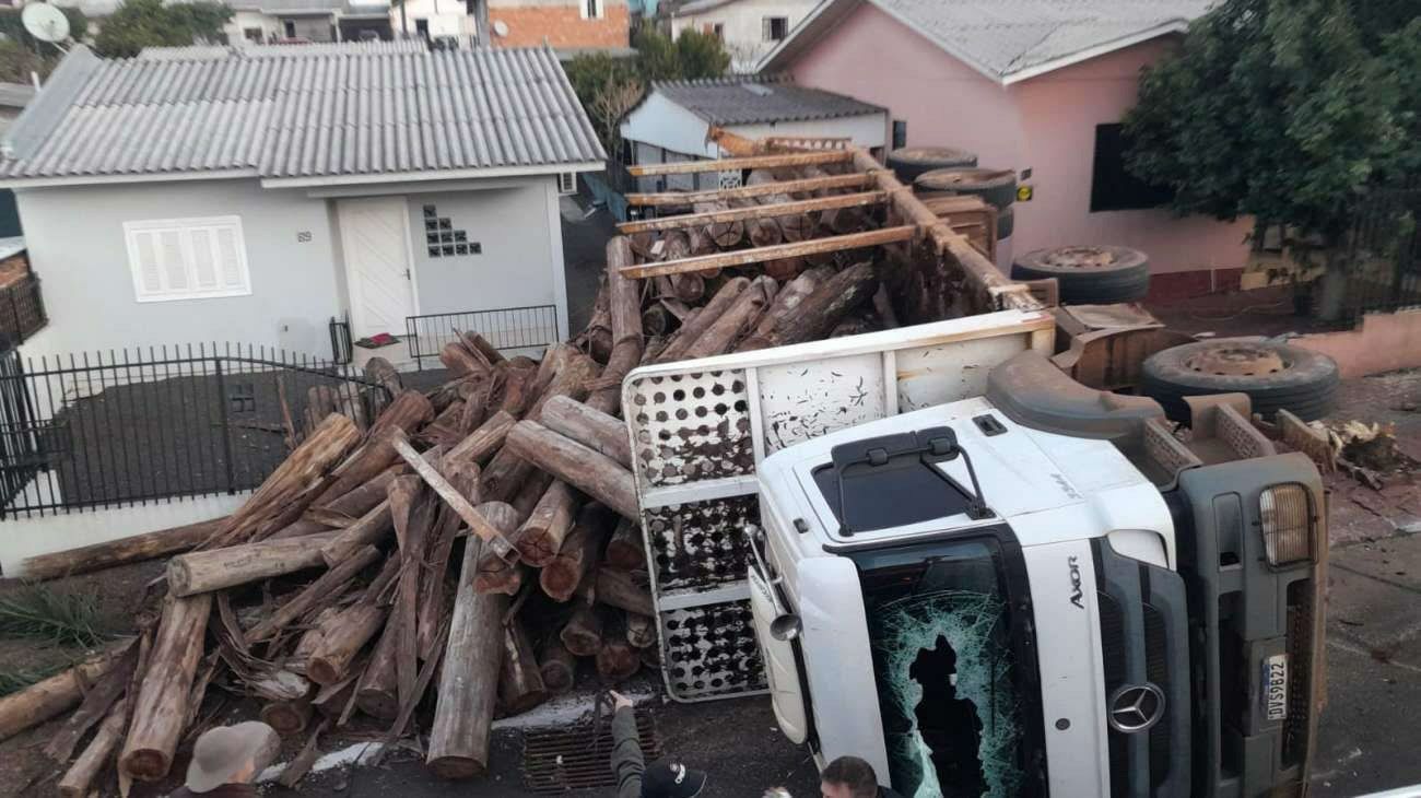 Caminhão com toras de madeira tomba, invade residências e carga destrói automóvel em Tapejara